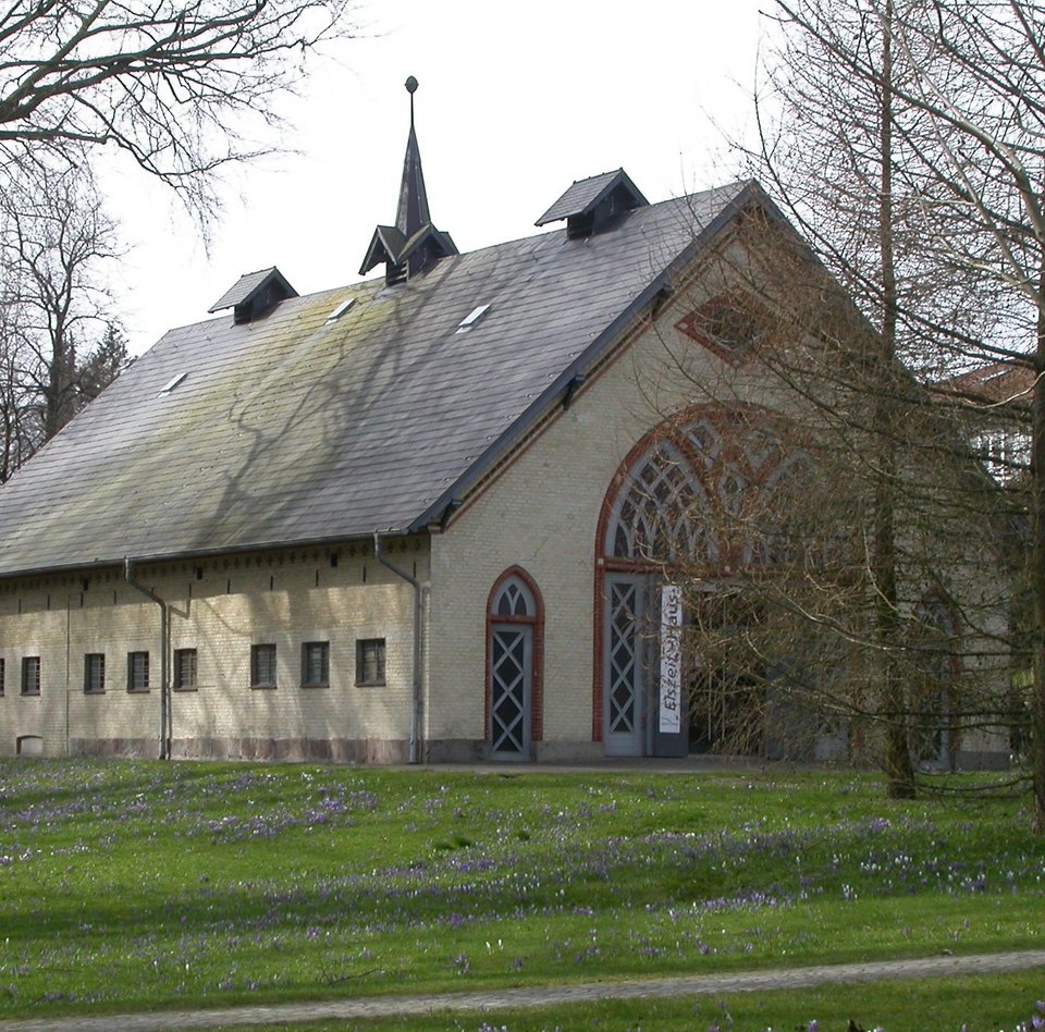 Das Foto zeigt das Eiszeit-Haus im Christiansenpark. Das rund 200 Jahre alte Gebäude war früher ein Pferdestall. Es ist aus gelblichen Ziegeln gebaut, rote Ziegel umranden die Türen. Das Spitzdach ist mit Schieferplatten gedeckt.