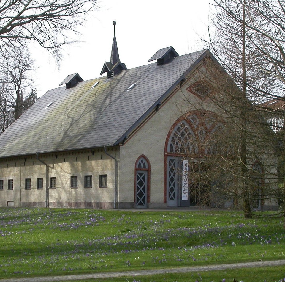 Das Foto zeigt das Eiszeit-Haus im Christiansenpark. Das rund 200 Jahre alte Gebäude war früher ein Pferdestall. Es ist aus gelblichen Ziegeln gebaut, rote Ziegel umranden die Türen. Das Spitzdach ist mit Schieferplatten gedeckt.