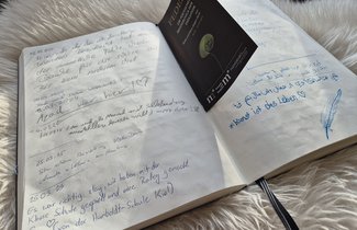 Das Foto zeigt den Blick in das aufgeschlagene Gästebuch der Museen. Das Buch liegt auf einem künstlichen, weißen Fell.