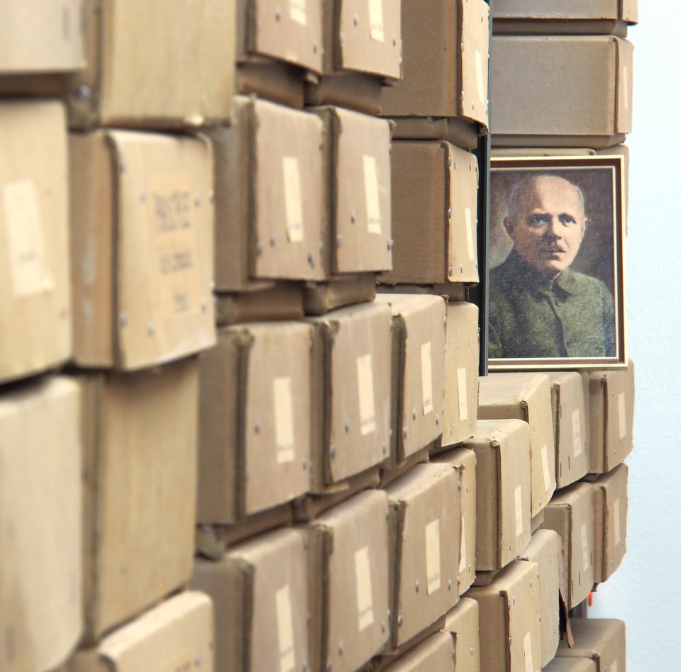 Das Foto zeigt viele beschriftete Sammlungskästen. Der Blick wird aber gelenkt auf ein gemaltes Portrait von Walter Saxen. Er hat die Flechten gesammelt, die sich in den abgebildeten Kästen befinden.