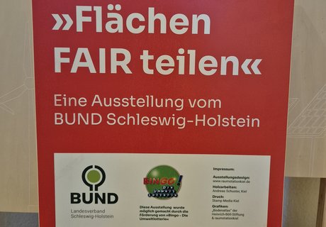 Das Foto zeigt einen Holzaufsteller mit Texttafel. Auf der Texttafel sind der Name der Wanderausstellung sowie die Gestalter als auch Sponsoren abgebildet. 