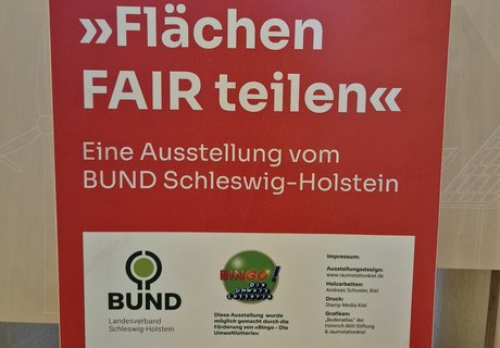 Das Foto zeigt einen Holzaufsteller mit Texttafel. Auf der Texttafel sind der Name der Wanderausstellung sowie die Gestalter als auch Sponsoren abgebildet. 