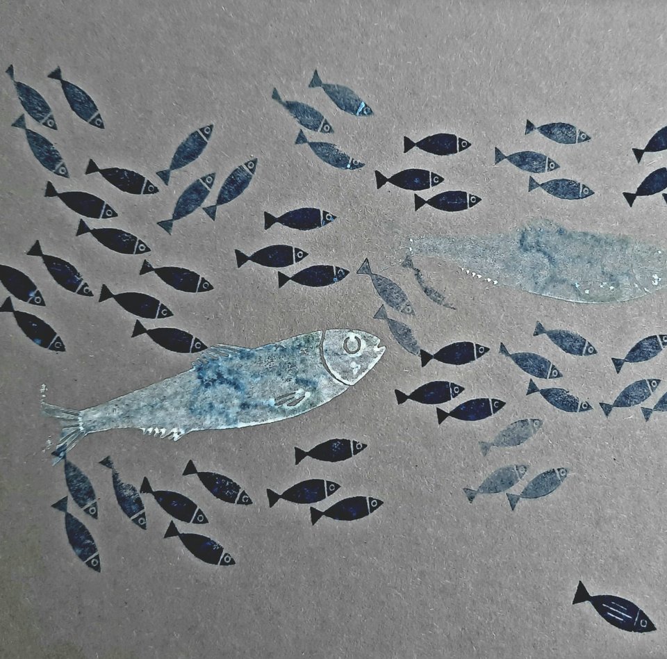 Auf dem Foto sind große und kleine Fische auf grauen Karton zu sehen. Die Fische wurden in verschiedenen Blau- und Silbertönen gestempelt. Sie schwimmen alle in die gleiche Richtung. 