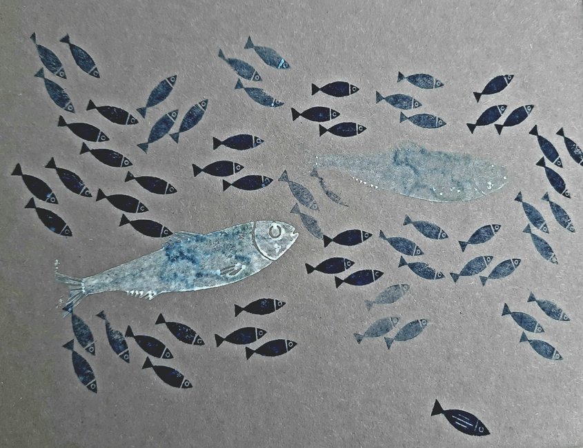 Auf dem Foto sind große und kleine Fische auf grauen Karton zu sehen. Die Fische wurden in verschiedenen Blau- und Silbertönen gestempelt. Sie schwimmen alle in die gleiche Richtung. 