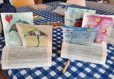 Das Foto zeigt die Ergebnisse einer Kreativwerkstatt. Es handelt sich um Zettelhalter aus Büchern mit selbst gestalteten, bunten Zeichnungen darin.