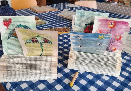 Das Foto zeigt die Ergebnisse einer Kreativwerkstatt. Es handelt sich um Zettelhalter aus Büchern mit selbst gestalteten, bunten Zeichnungen darin.