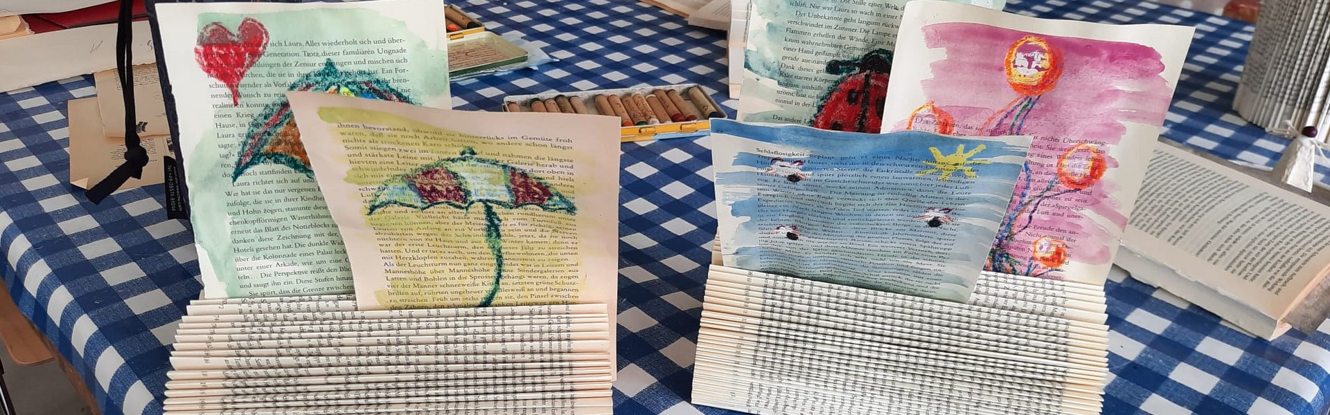 Das Foto zeigt die Ergebnisse einer Kreativwerkstatt. Es handelt sich um Zettelhalter aus Büchern mit selbst gestalteten, bunten Zeichnungen darin.